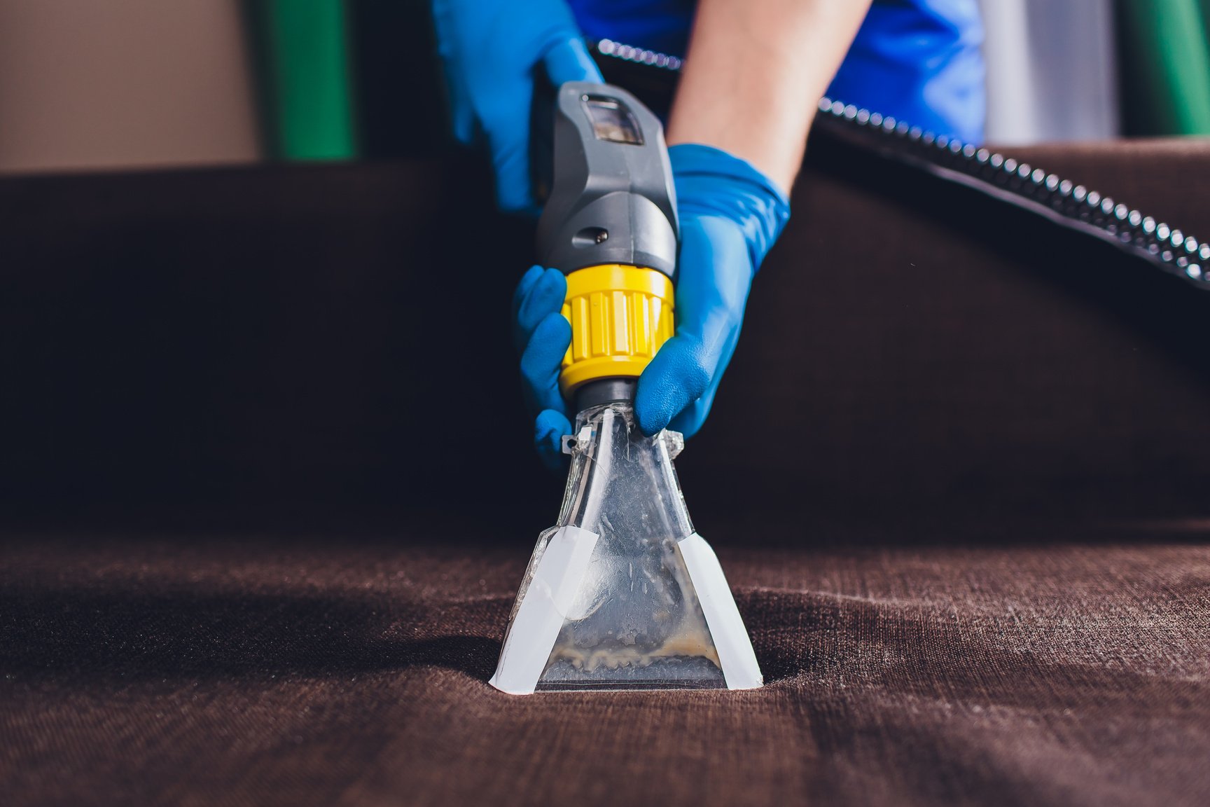 Sofa chemical cleaning with professionally extraction method. Upholstered furniture. Early spring cleaning or regular clean up. Dry cleaner's in protective glove employee removing dirt from furniture in flat.